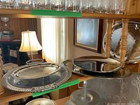Photo of various metal serving trays on shelf showing reflective oval trays and round tray with smooth and decorative edges.