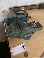 Three metal bench vises arranged on a wooden surface, showing different sizes and wear.