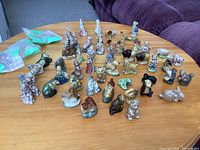 Overview of the full collection of miniature ceramic animal and character figurines arranged on a wooden table showing diverse designs and colors.