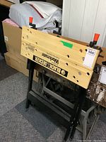 Photo showing the front view of the Black & Decker Workmate workbench, highlighting the wooden top with branding and orange clamp handles.