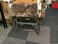 Front view of work bench showing wooden top with paint stains and metal frame.