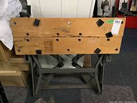 Front view of wooden work bench top with multiple black plastic clamps and metal frame legs underneath.