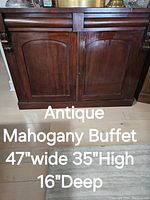 Photo showing the antique mahogany buffet cabinet's front view with two paneled doors and a dark finish on a wood floor.