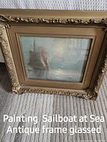 Photo of antique framed painting showing a sailboat at sea behind glass, with ornate carved frame details.