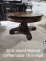 Round walnut coffee table with central pedestal base and curved feet, shows overall appearance.