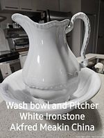 White ironstone wash bowl and pitcher set with scalloped edges and detailed handle, placed on a kitchen counter.