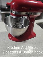 Red KitchenAid Ultra Power stand mixer on countertop with stainless steel mixing bowl attached. Wire whisk beater attached. Text in image states 'Kitchen Aid Mixer. 2 beaters & Dough hook'.