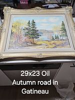 Oil painting showing an autumn road in Gatineau with lake and trees, framed in a decorative cream frame.