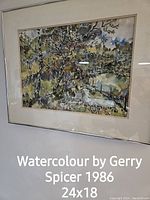 Photo of a framed watercolour painting by Gerry Spicer from 1986, showing a landscape scene with trees and natural elements in a glass covered frame.
