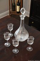 Full view of the antique etched glass sherry decanter with stopper and four matching sherry glasses arranged around it on a table.