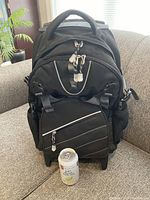 Front view of the black carry-on knapsack showing zippered compartments, front pockets, and attached key rings with a reference can for size.