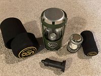 View of both UCO camping lanterns with their respective black foam protective cases on beige carpet.