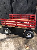 Side view of wooden wagon showing red rails and rubber tires on paved ground.