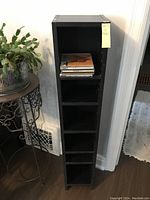 Front view of black CD holder tall and slim with 4 shelves, 4 CDs placed on one shelf