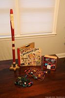 Tall skinny wooden Santa, vintage Nutcracker Suite album, two sets of vintage Christmas lights and a box of colorful ornaments on a table