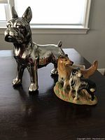 Photo showing two dog novelty items: the larger silver dog figurine and the smaller colorful dog matchstick holder.