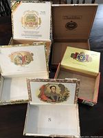 Five wooden cigar boxes opened to show detailed internal brand artwork on lids, including Churchill and Bolivar.