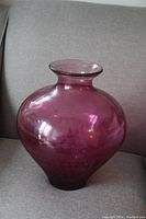 Photo of the fuscia-colored glass vase showing bulbous shape and flared mouth taken on a grey couch.