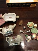 Photo showing three-piece grey ceramic elephant set with floral decoration, small armadillo figurine, miniature mouse tea set components including cups and plates, and three small mouse figurines