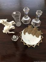 Top down view of all items: pair of glass candlesticks, etched glass vase, perfume bottle, horse figurine, and milk glass kitten plate.