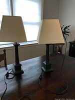 Photo showing the pair of table lamps on a wooden table near a window, displaying their full height and shape.