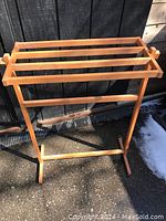 Front angle view of the wooden quilt stand showing four horizontal rungs and frame supporting base.