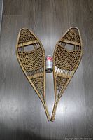 Pair of vintage wooden snowshoes with gut lacing displayed flat on wooden floor with a Diet Coke can for size reference.