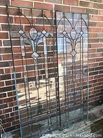 Front view of two tall caned glass panels leaning against brick wall showing clear glass panes and cane outlines, some cracked and missing pieces.