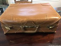 Top view of brown leather suitcase showing worn surface and metal closers on front edge.