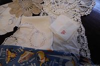 View of assorted vintage linens including crocheted doilies, embroidered linen pieces, and colorful 1939 NY World's Fair scarf laid out on table
