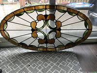 Full view of the oval vintage stained glass panel with green, amber, and clear textured glass.