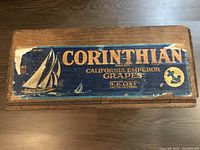 Top view of the vintage wooden crate showing the Corinthian brand label with a sailboat graphic and grape branding.