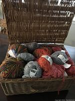 Open wicker basket filled with various yarn balls of different colors and textures from several brands