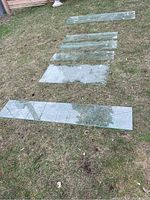 Overview of six clear glass table tops laid out on grass showing different lengths and widths.