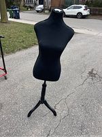 Full view of black female bust dress form on a detachable tripod stand outside.
