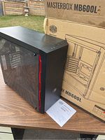 Cooler Master MasterBox MB600L ATX mid-tower case displayed on table outdoors with original box and manual behind it.