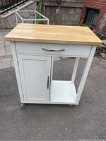 Front and side view of the white rolling cart cabinet showing wood top, drawer, cabinet door, open shelf, and caster wheels.