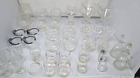 Photo of the entire collection of varied glassware including different types of glasses, small bowls, and bottles arranged across a white surface.