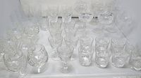 Photo of various crystal glasses showing cocktail, wine, water, drink, and cognac glasses arranged together on a white surface.