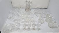 Photo of the full crystal glassware set arranged showing various glasses, plates, bowls, creamer, napkin holder and carafe, all clear glass with decorative etched patterns.