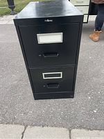 Front view of black metal filing cabinet showing two drawers with label holders and handles.