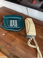 Green retro push button phone and cream handheld phone on wooden surface
