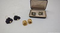 Photo showing three pairs of earrings and cufflinks, including black puff earrings on left, gold tone ribbed earrings in center, and Stetson cufflinks in box on right.