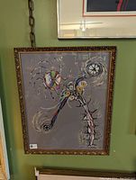 Photo showing framed abstract artwork with colorful circular and linear patterns on a gray background.