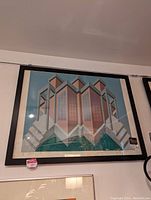 Framed geometric print featuring abstract architectural design in blue, pink, and brown tones, signed by the artist.