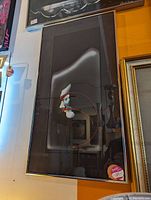 Framed abstract art print with dark matte background and curved lines in white, red, and gray tones. Photo taken to show the entire artwork and framing condition.