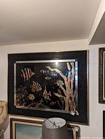 Framed fish art on a wall with dark background and vibrant, colorful fish and aquatic plant designs.