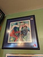 Framed limited edition serigraph art print on a wall with protective stickers visible on glass and frame.