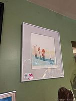 Framed serigraph print showing an illustration of a person with skis, mounted on a pale green wall