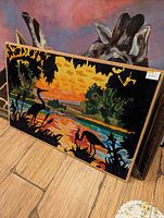 Needlepoint artwork panel showing a sunset with birds and plants in silhouette.
